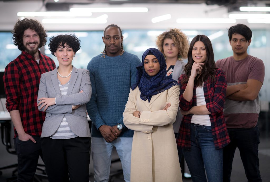 portrait of young excited multiethnics business team of software developers standing and looking at camera while celebrating success at modern startup office